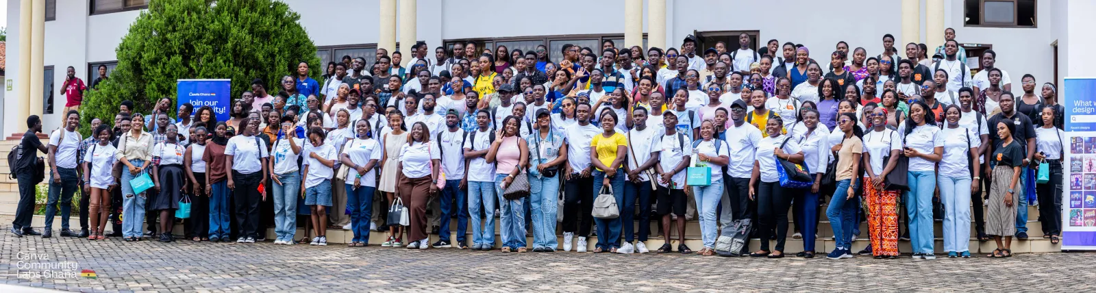 A large crowd of Canva Community Labs attendees, most in white event shirts, posing for a group photo on the steps of a pillared venue in Accra.